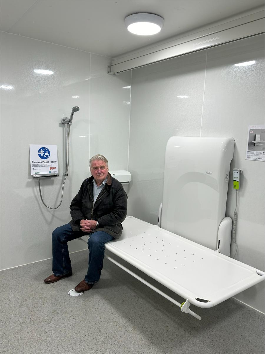 Cllr Bill Hunt is pictured sitting on the drop-down changing bed in the Changing Places toilet